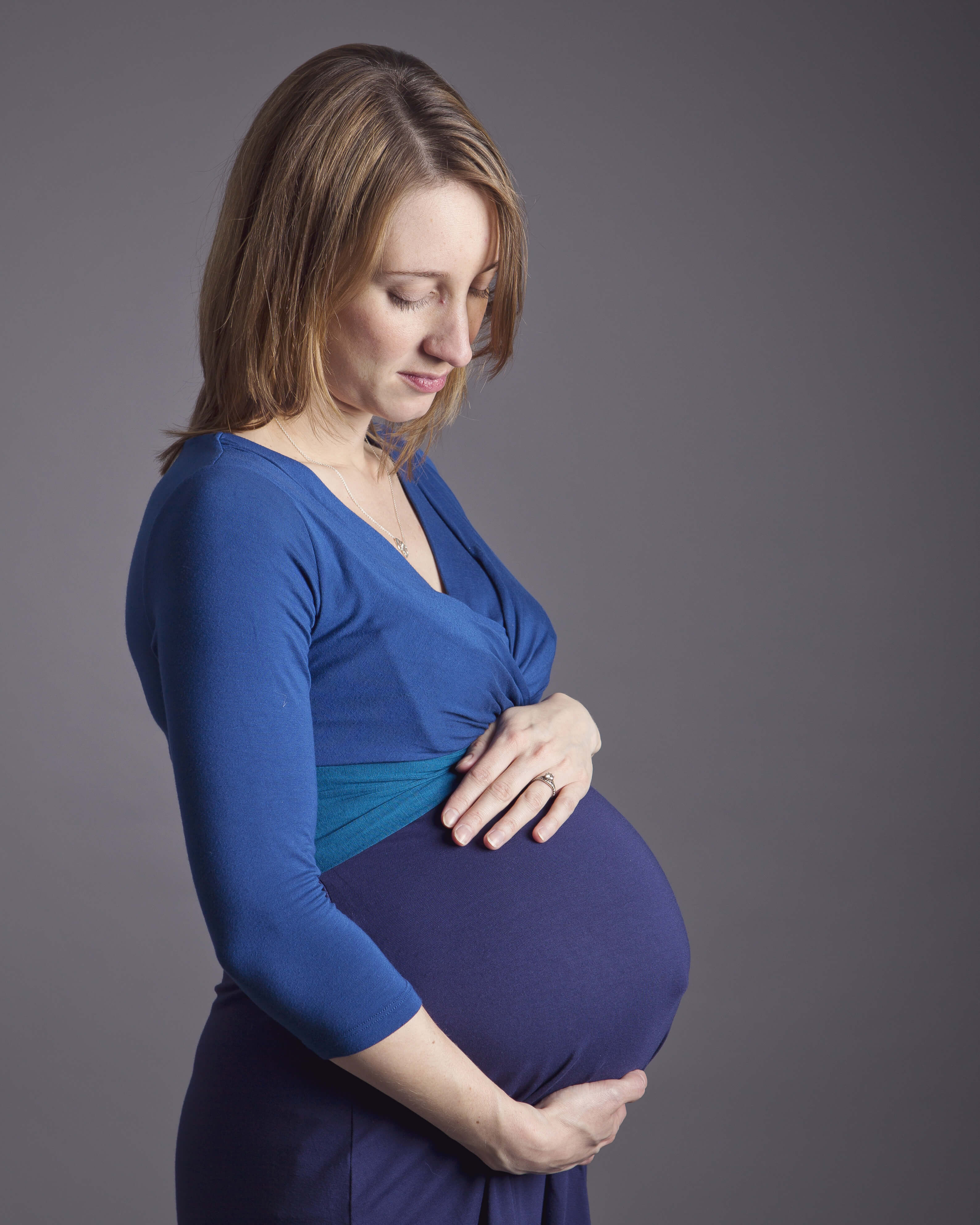 woman in blue dress looking at baby bump by maternity photographer Winchester