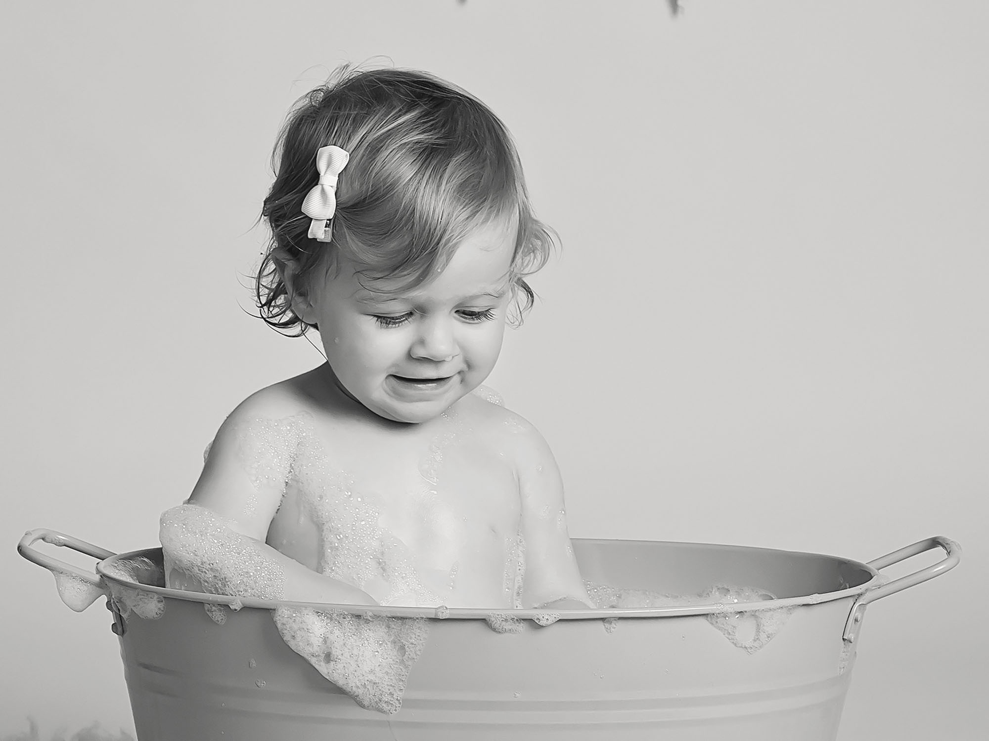 black and white photo of baby girl in bubble bath by cake smash photographer Winchester