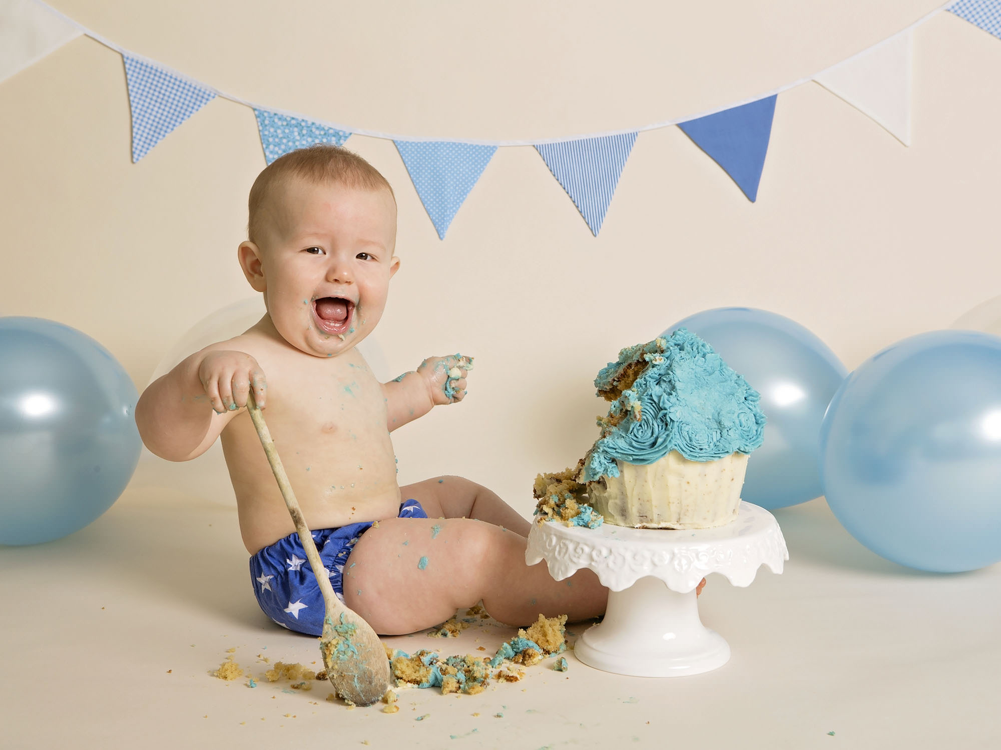 boy using wooden spoon to smash cake by cake smash photographer Winchester