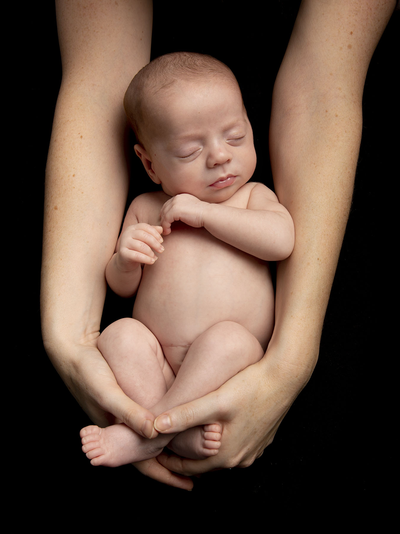 baby in mums arms on black background by Winchester newborn photographer